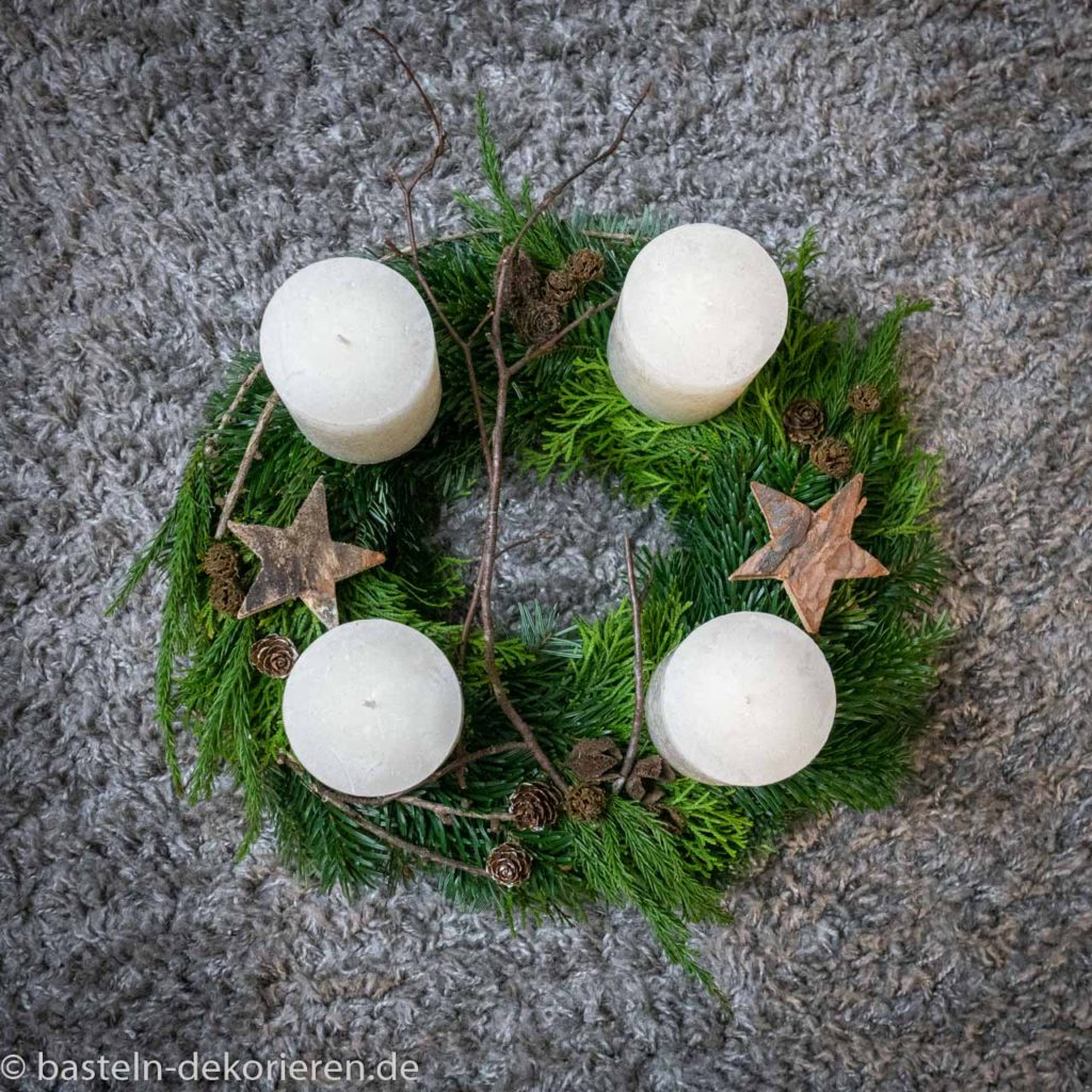 Adventskranz 2019 mit Zweigen der Tanne, Thuja und Sicheltanne. Dekoriert mit weißen Kerzen, Holzsternen und Zapfen.