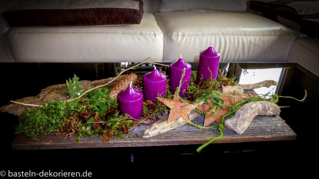 Adventskranz auf einem alten Brett mit Moos, Schwemmholz und Rost dekoriert.